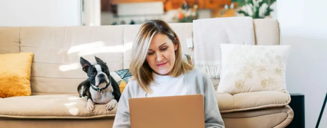 Woman at computer with dog in background on couch